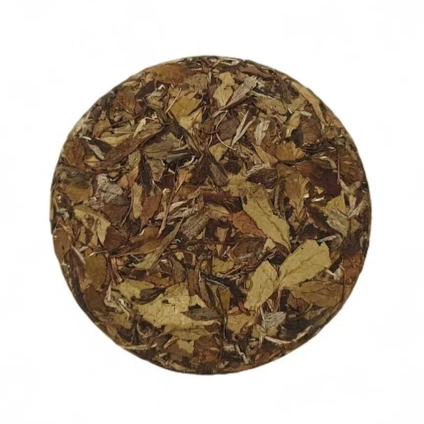 Round compressed tea cake with dried leaves on a white background