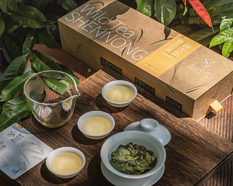 Tea set with 'Wild Tea Shennong' packaging on a wooden surface with white tea leaves.
